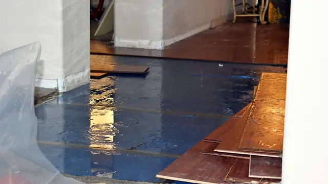 Wet hardwood planks lifted over plastic sheeting after a water leak