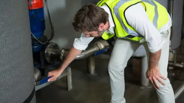 Technician in a safety vest checking a water heater and its connections for a leak